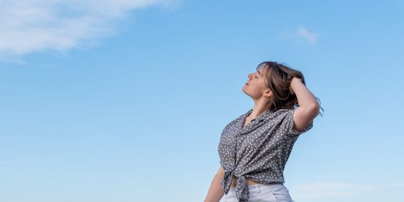 A beautiful young woman looks towards the sky, thoughtful, with her hands in her hair.